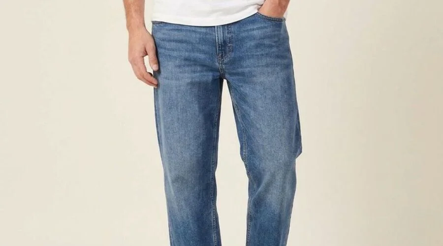 Model in mid-wash relaxed jeans standing casually, showing everyday wear creases