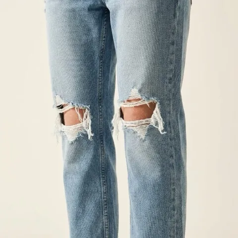 Close-up of jeans with a ripped knee showing frayed horizontal threads