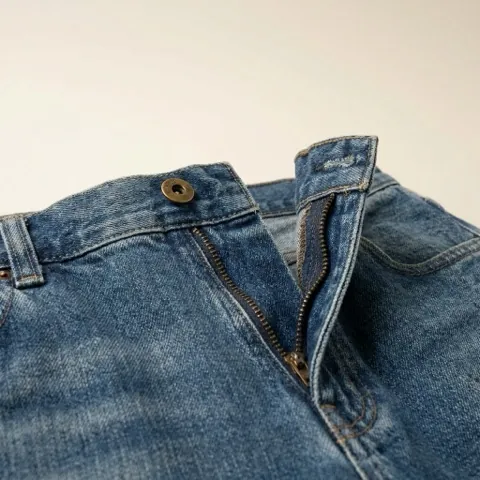 Close-up of a denim zip fly with a metal zip and shank button