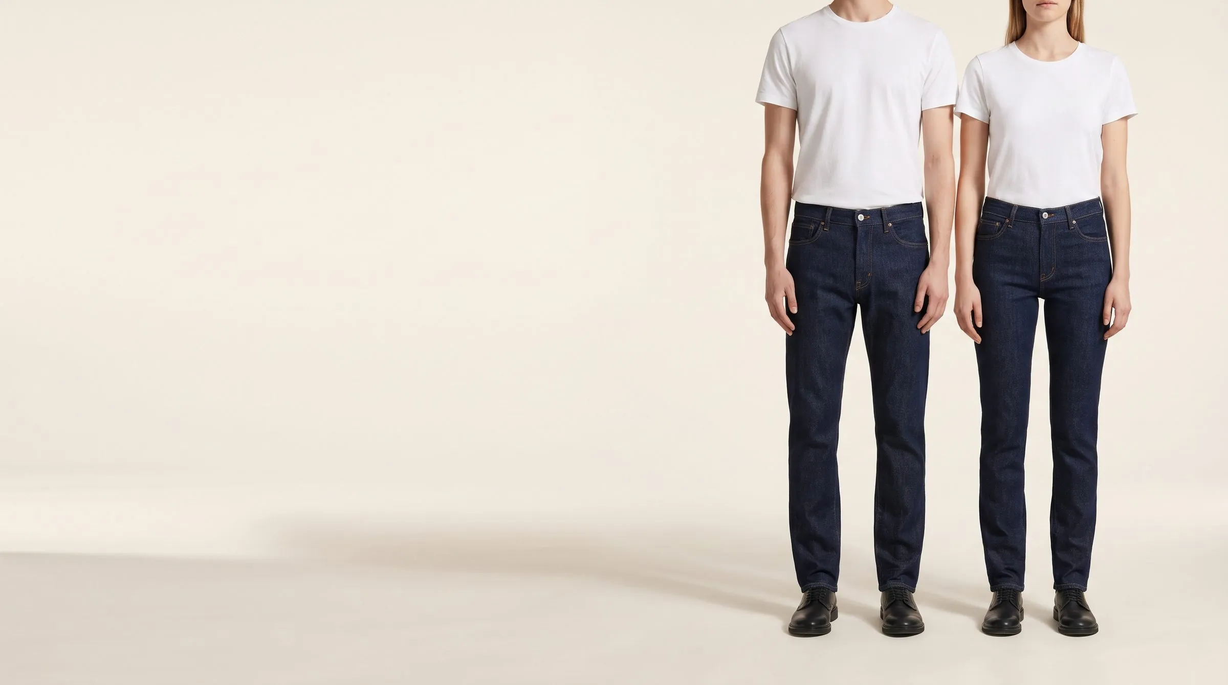 Mid-wash slim jeans laid long and flat on a cutting table, the tape running past the hem to show an extra-long inseam